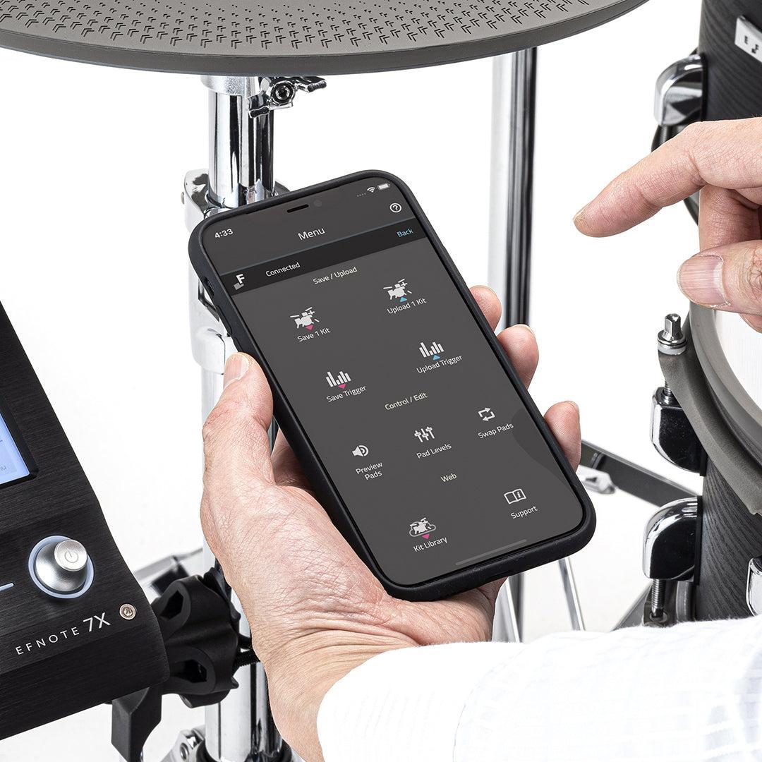 Person using a smartphone app to control the EFNOTE 7X e-drum set with drum pads and module visible