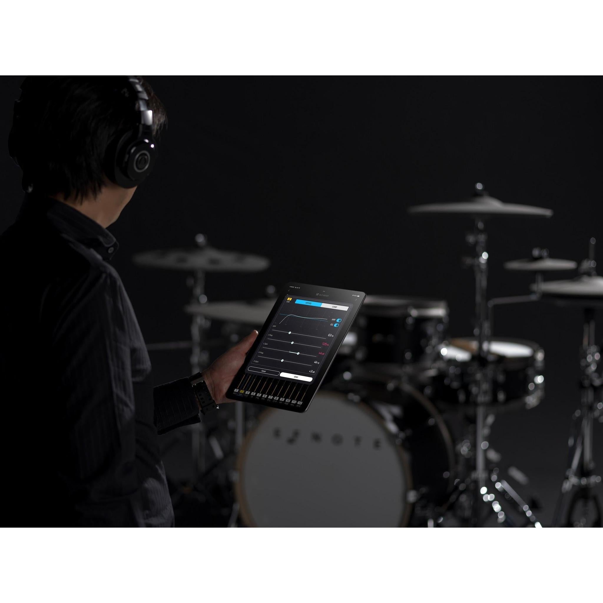 Person adjusting sound settings on a tablet near EFNOTE PRO 703X electronic drum kit in a dark studio setting