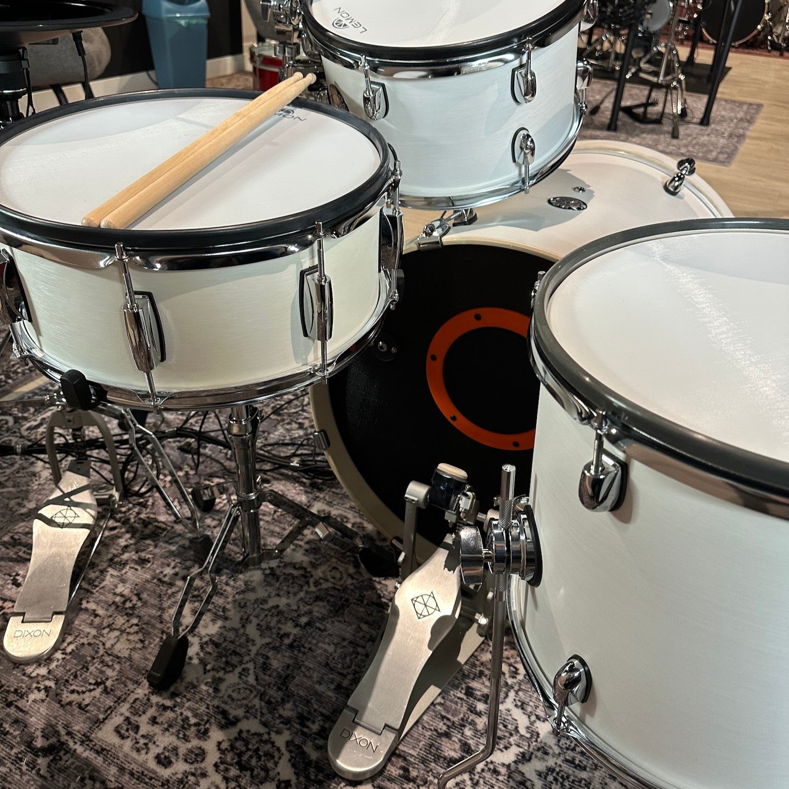 Lemon Fusion Shell Set white wooden drums with chrome hardware on patterned rug by Lemon vendor with drumsticks