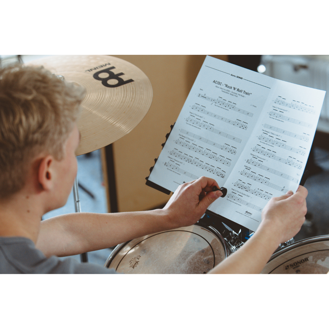 Person holding sheet music secured with NBO Magnet Pack for Oneboard while sitting at a drum set with cymbals visible