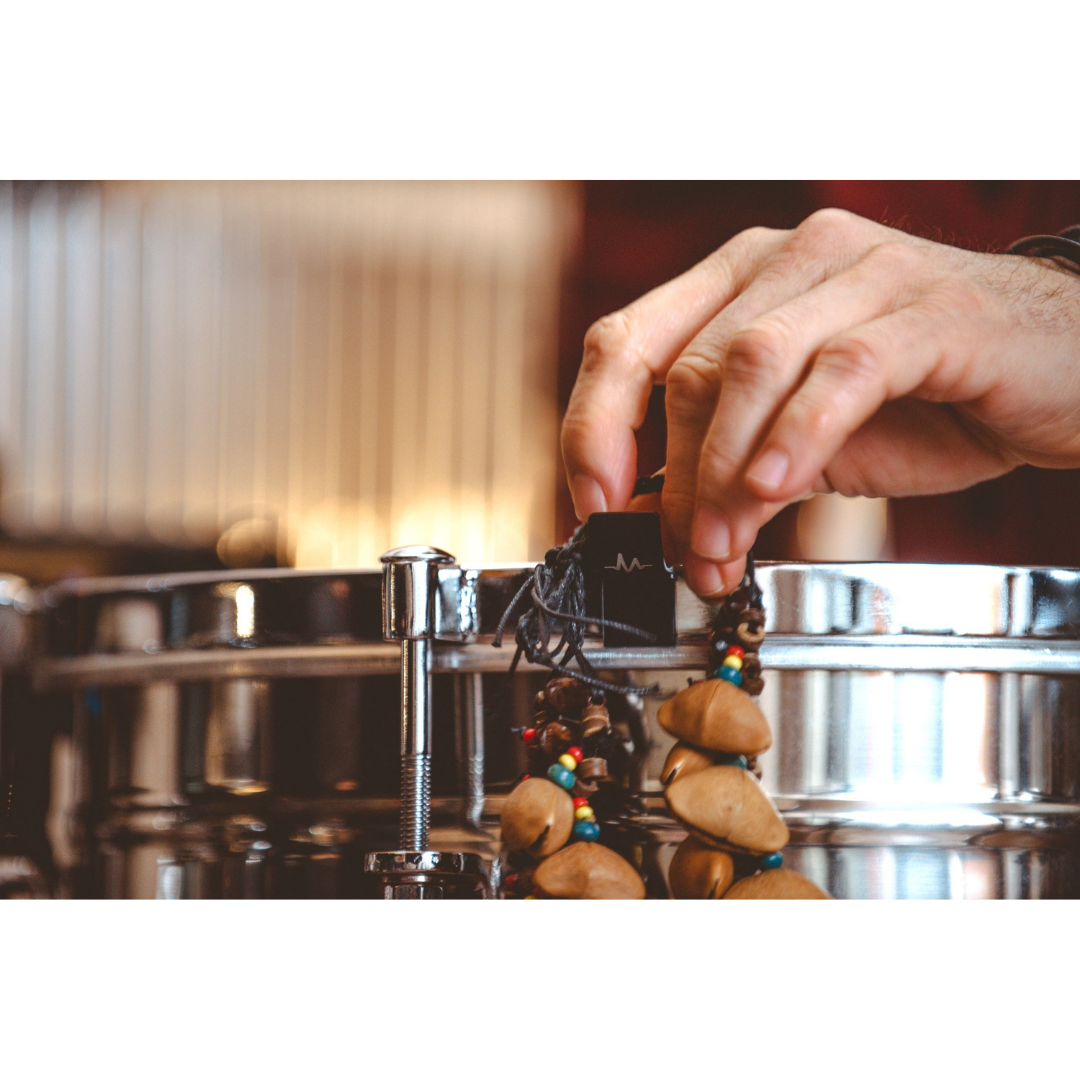 Hand placing a black L-shaped magnet from NBO Magnet Pack for Oneboard on a drum rim holding a beaded necklace