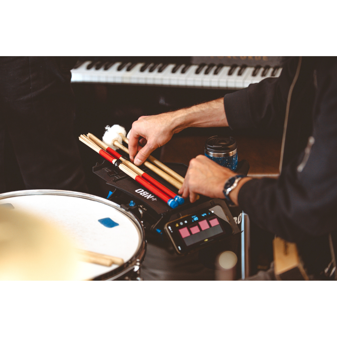 Musician arranging sticks on the NBO Standard Extension for Oneboard with drum and piano in background.