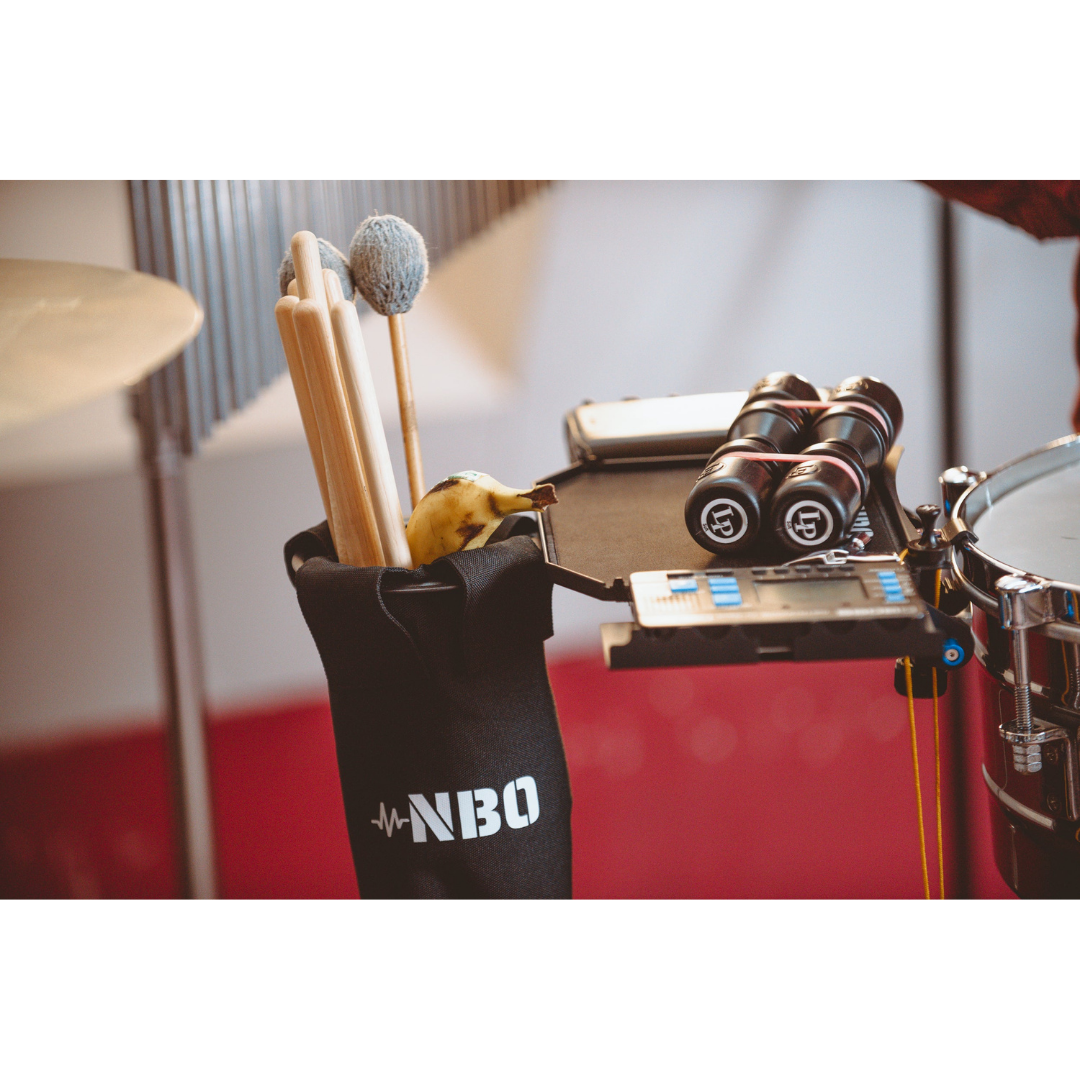 NBO Stick / Drink Holder for Oneboard attached to drum set holding sticks, mallets, and a banana with NBO logo visible.