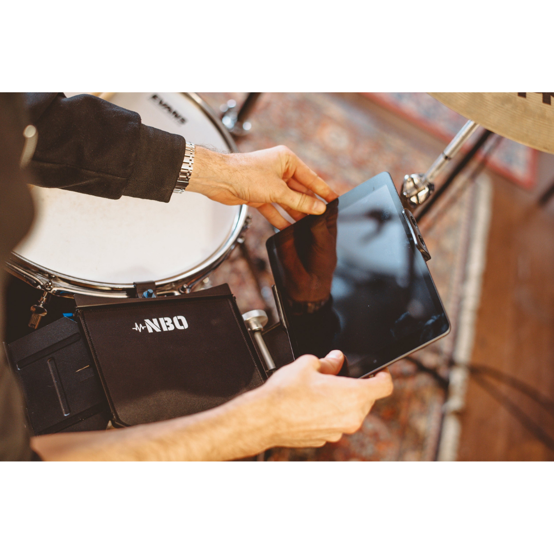 NBO Tablet/Phone Holder for Oneboard holding a tablet near a drum set with the NBO logo visible on the holder.